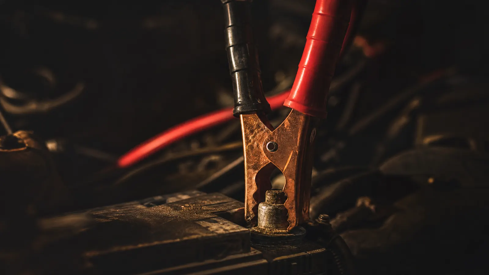 Jumper cable clamps biting onto a car battery terminal at night.